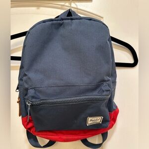 Blue color and a red bottom. The backpack features a zip closure in front